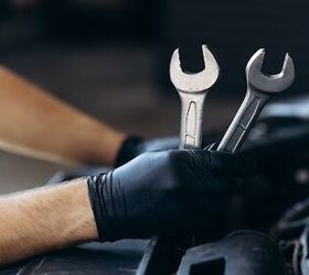 A man working on a car in a repair shop with two wrenches.
